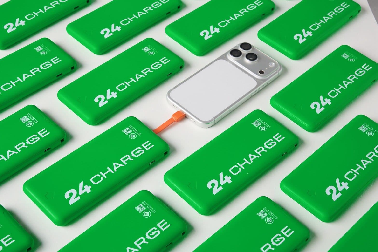 พาวเวอร์แบงก์ 24CHARGE เรียงทแยงเต็มเฟรม โดยมีโทรศัพท์หนึ่งเครื่องเสียบสายชาร์จสีส้มอยู่ตรงกลาง