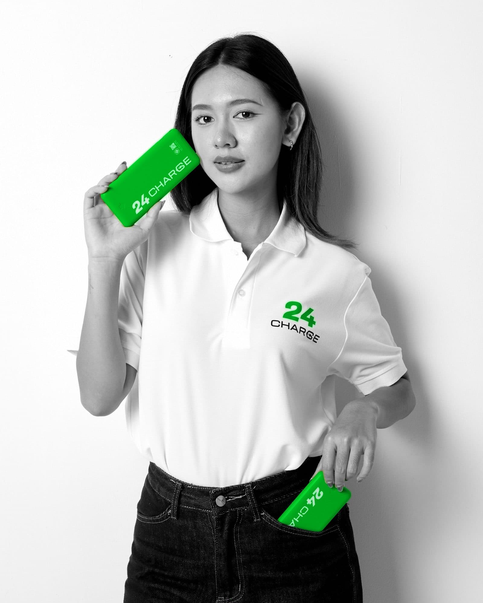 ภาพขาวดำที่คงสีเขียวไว้เฉพาะสินค้า: ผู้หญิงถือพาวเวอร์แบงก์ 24CHARGE สีเขียวสองตัวข้างใบหน้าและที่กระเป๋ากางเกง