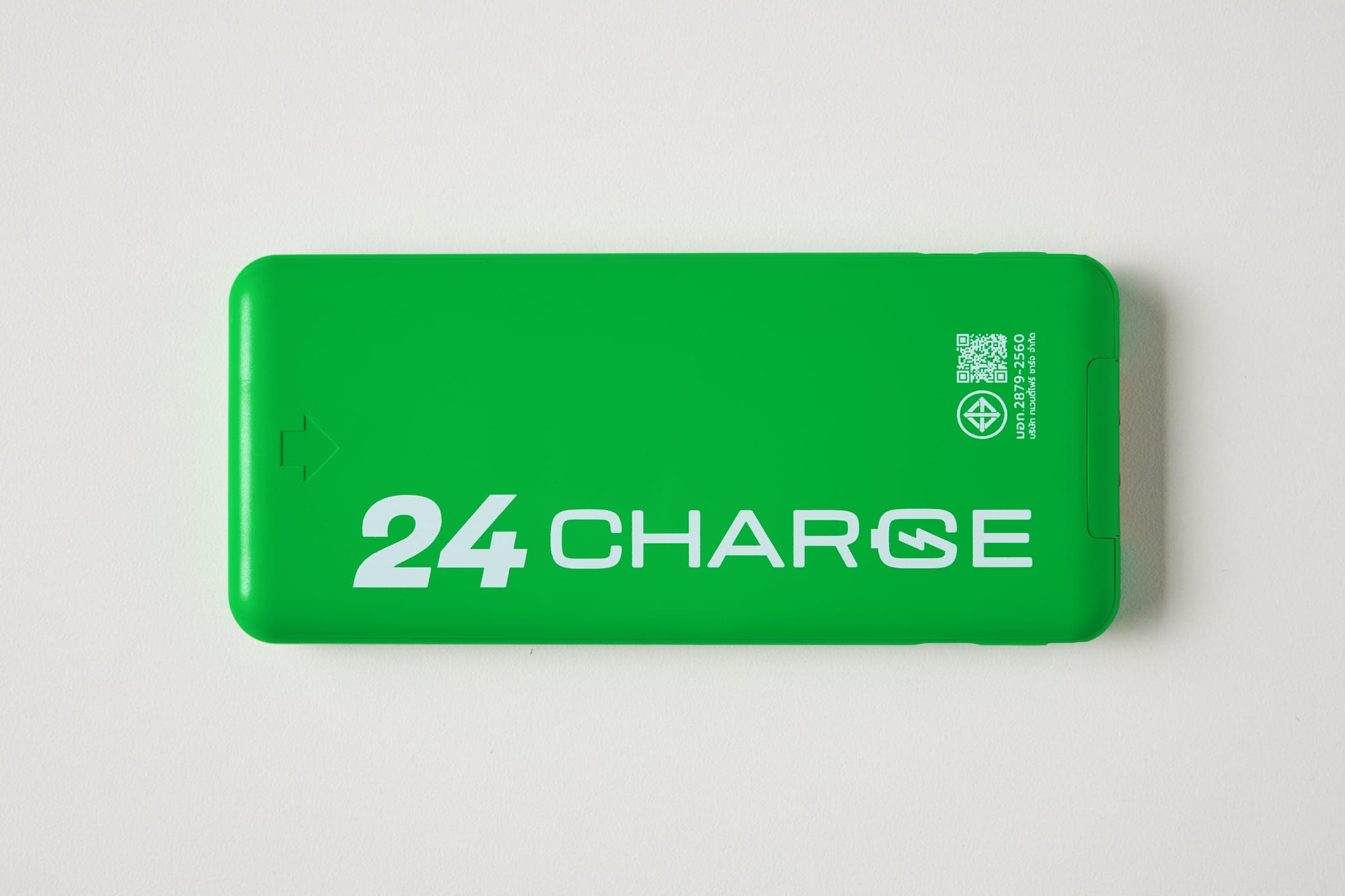 พาวเวอร์แบงก์ 24CHARGE มุมมองที่ 1 มุมถ่ายจากด้านบนตรงลงมา เห็นด้านหน้าตัวเครื่องพร้อมโลโก้ 24CHARGE ไอคอนลูกศร และ QR โค้ดพร้อมตราสัญลักษณ์รับรองมาตรฐาน บนพื้นหลังสีขาว